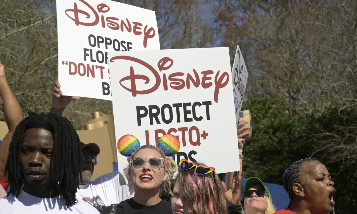 Pessoas protestando segurando cartazes com o logo da Disney em defesa da comunidade LGBTQ+.